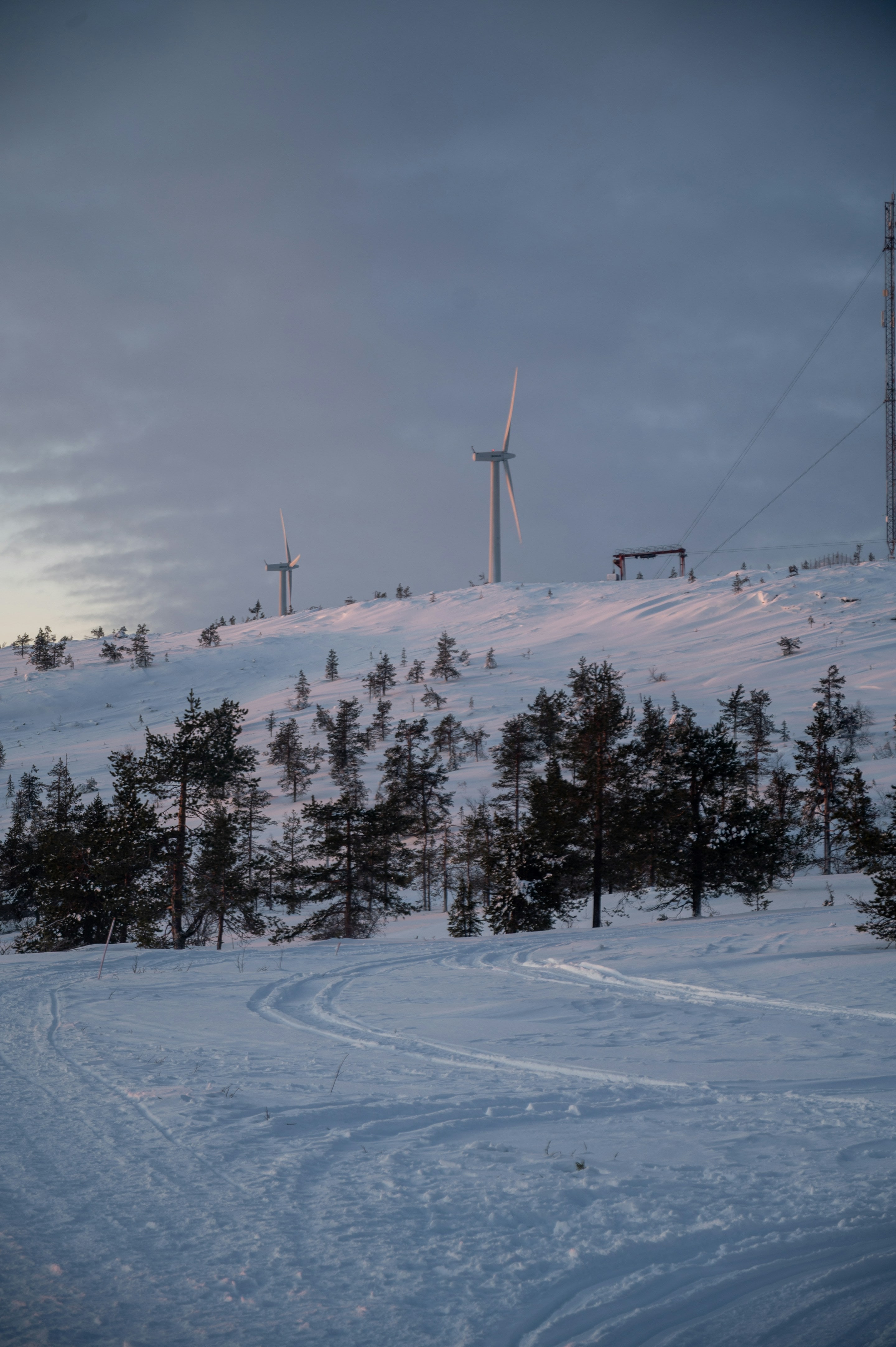 Wind turbines on a snowy Nordic hillside at dawn